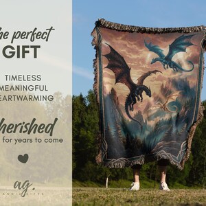 May include: A tapestry blanket featuring a fantasy scene with three dragons soaring over a mountainous landscape. The blanket has a fringed edge and is held up against a blue sky. The text on the left side says "The perfect GIFT".