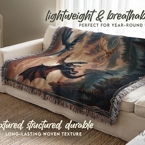 May include: A woven throw blanket featuring a fantasy scene with dragons in flight. The blanket has a detailed illustration in shades of blue, brown, and orange. The text "lightweight & breathable" and "textured, structured, durable" is visible.