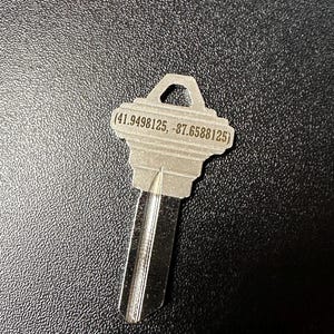 May include: A silver key with a small loop at the top and the coordinates (41.9498125, -87.6588125) engraved on the top.