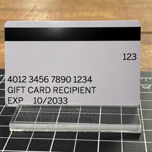 Puede incluir: Una tarjeta de regalo blanca con texto negro. La tarjeta tiene una banda magn&eacute;tica negra y el n&uacute;mero 123 impreso en la esquina superior derecha. El texto en la tarjeta dice "4012 3456 7890 1234 GIFT CARD RECIPIENT EXP 10/2033".