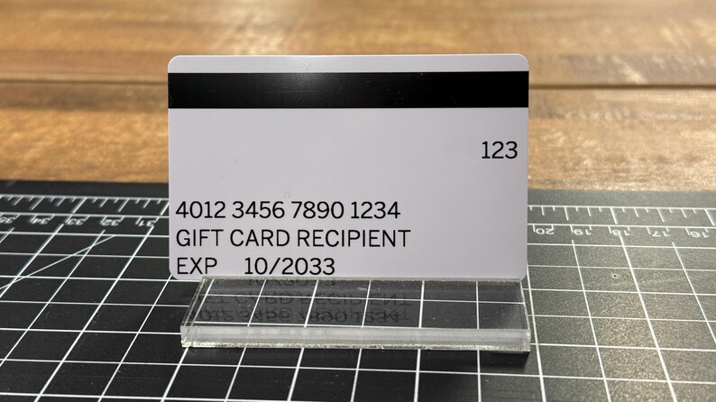 Puede incluir: Una tarjeta de regalo blanca con texto negro. La tarjeta tiene una banda magn&eacute;tica negra y el n&uacute;mero 123 impreso en la esquina superior derecha. El texto en la tarjeta dice "4012 3456 7890 1234 GIFT CARD RECIPIENT EXP 10/2033".