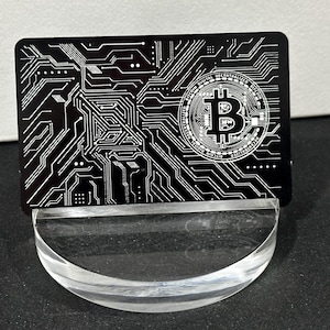 May include: A black metal card with a white circuit board design and a white Bitcoin logo in the center.