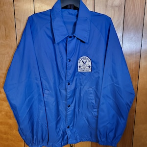 May include: A blue nylon jacket with a Boy Scout Troop 148 Eagle patch. The patch features a white eagle with a blue background and the text "Boy Scout Troop 148 Eagle Arlington, Virginia Formed 1950".