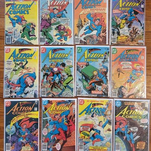 Puede incluir: Una colección de cómics antiguos de "Action Comics" con Superman. Las portadas de los cómics muestran ilustraciones vibrantes de Superman en acción, luchando contra villanos y salvando el mundo. Los cómics están en fundas protectoras.