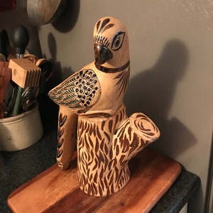 May include: A ceramic bird figurine with brown, green, and black painted details, perched on a brown and black ceramic tree stump.