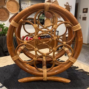 May include: A vintage, handcrafted rattan magazine rack. The rack features a circular design with multiple interconnected rings and a curved base. The natural brown color of the rattan is accented by lighter-toned woven details, creating a decorative and functional piece.
