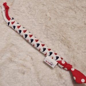 Könnte beinhalten: Ein Stoffspielzeug mit einem Muster aus roten und marineblauen Walen auf weißem Grund. Es hat ein rot-weißes Seil an einem Ende und einen roten Polka-Dot-Knoten am anderen. Ein Etikett mit "la-maco" ist angebracht.