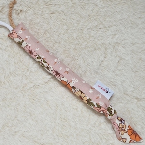 Könnte beinhalten: Ein rosa Katzenspielzeug mit Blumenmuster und einem Seilgriff. Das Spielzeug besteht aus Stoff mit einem sich wiederholenden Blumenmuster in Rosa-, Orange- und Weißtönen. Das Etikett lautet "la-maco".