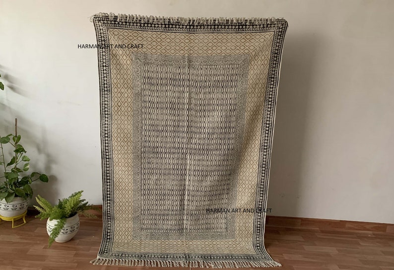 Puede incluir: Una alfombra con estampado en blanco y negro con flecos en los bordes. La alfombra tiene un dise&ntilde;o geom&eacute;trico y est&aacute; hecha de algod&oacute;n. La alfombra est&aacute; sobre un suelo de madera.