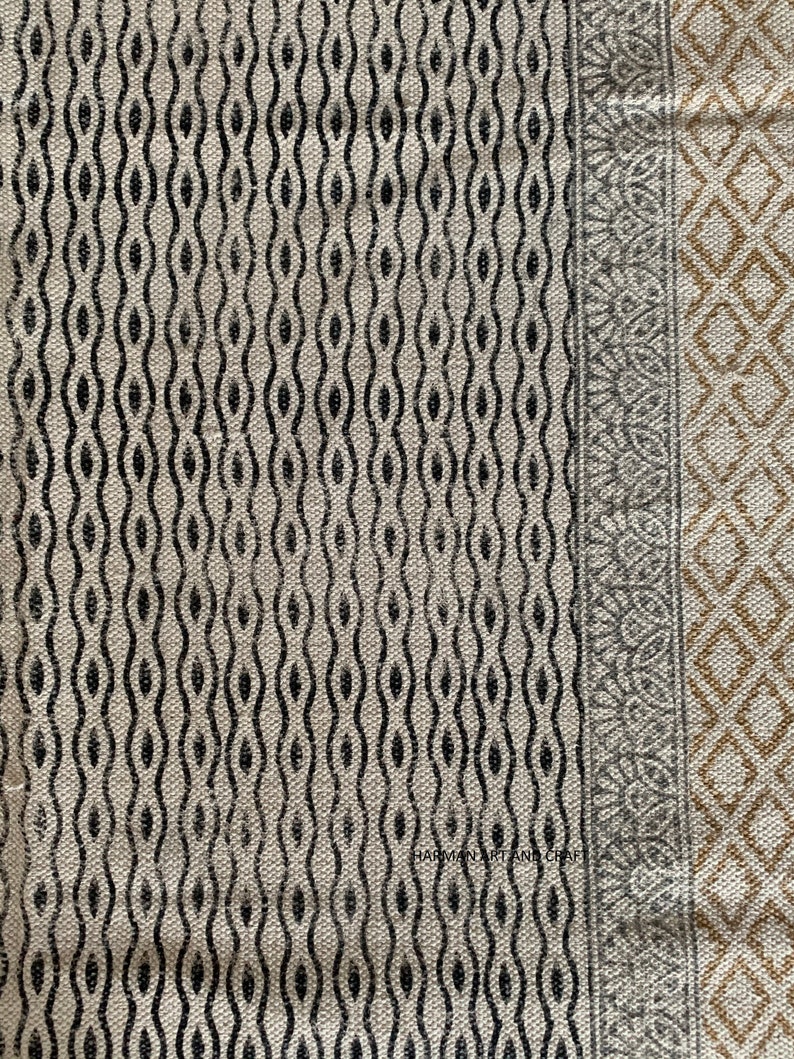 Puede incluir: Primer plano de una tela beige con un patr&oacute;n geom&eacute;trico en blanco y negro. La tela tiene un borde con un patr&oacute;n geom&eacute;trico gris y dorado. El texto "HARMAN ART AND CRAFT" es visible en la esquina inferior izquierda.