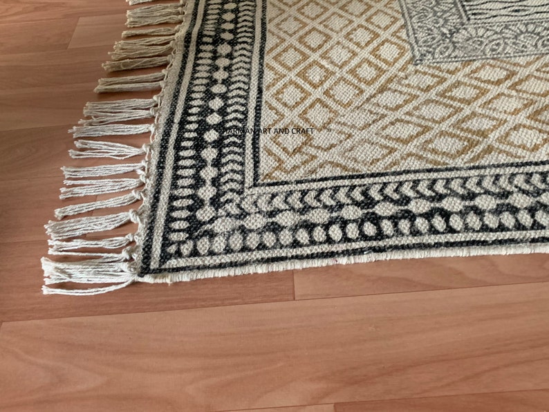 Puede incluir: Una alfombra blanca y negra con un borde de flecos. La alfombra tiene un dise&ntilde;o geom&eacute;trico con detalles en blanco y negro.