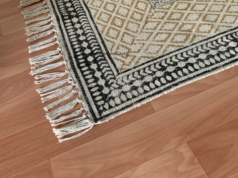 Puede incluir: Una alfombra blanca y negra con un borde de flecos. La alfombra tiene un dise&ntilde;o geom&eacute;trico con diamantes blancos y negros y un borde marr&oacute;n y blanco.