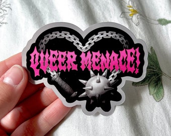 Puede incluir: Una pegatina en forma de corazón rosa y negro con el texto "Queer Menace!" en una fuente gótica en negrita. El corazón está rodeado de una cadena y presenta una maza con púas y una daga.