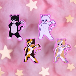 Op de afbeelding: Vier kleurrijke katten stickers op een roze achtergrond. De katten staan in een danspose met hun armen uitgestrekt. De stickers zijn op een roze achtergrond met witte sterren.