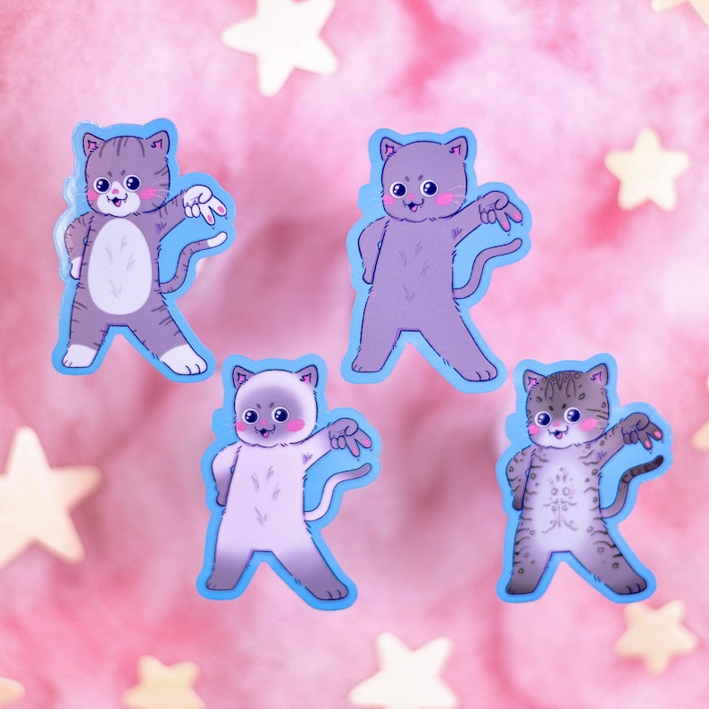 Op de afbeelding: Vier kleurrijke katten stickers met blauwe contouren. Elke kat staat in een andere pose met een speelse uitdrukking. De stickers zijn op een roze achtergrond met witte sterren.