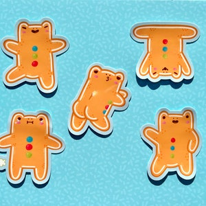 Puede incluir: Cinco pegatinas de rana de jengibre con decoraciones de caramelo de colores. Las ranas están en varias poses, incluyendo de pie, sentadas y boca abajo.