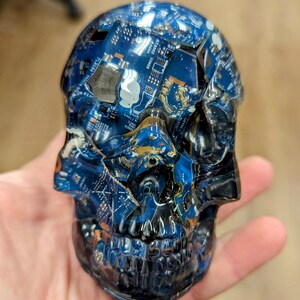May include: A blue and black skull sculpture made from recycled circuit boards. The skull is detailed with a realistic face and teeth.