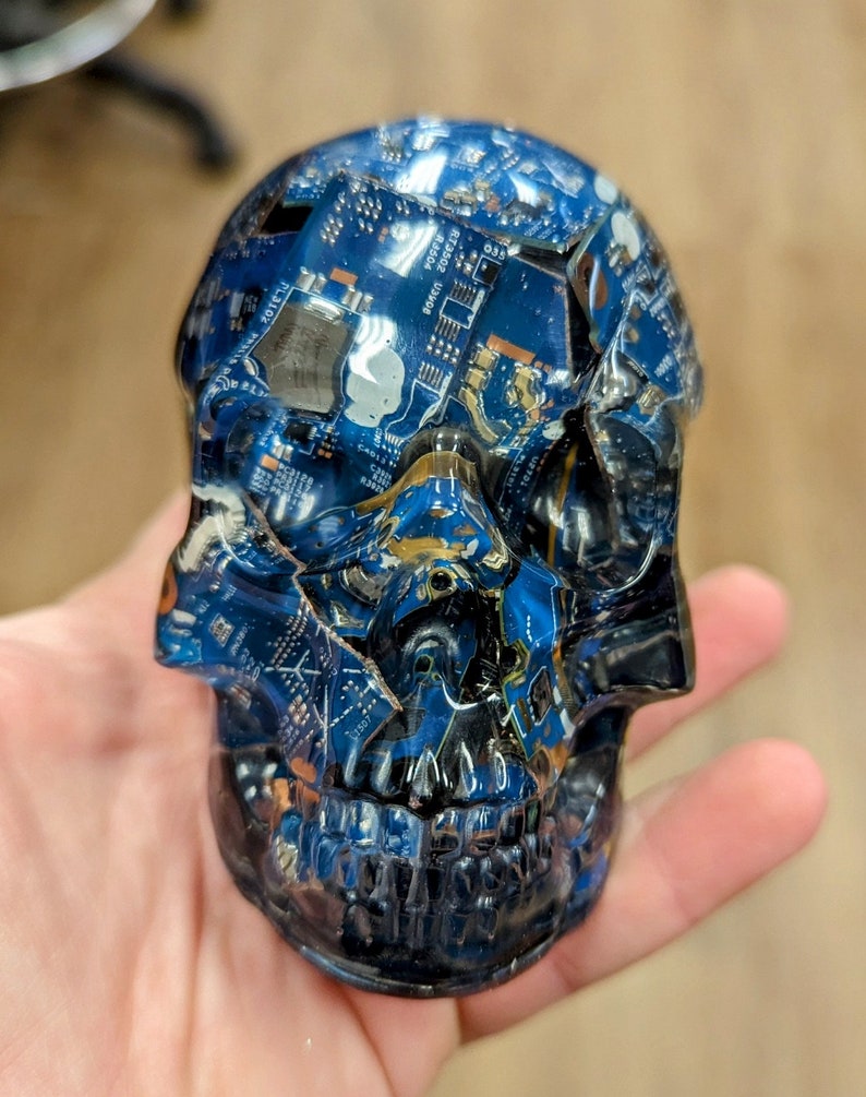 May include: A blue and black skull sculpture made from recycled circuit boards. The skull is detailed with a realistic face and teeth.