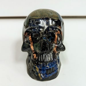 May include: A black resin skull sculpture with embedded circuit boards and copper wiring. The skull is detailed with a black resin jaw and teeth.