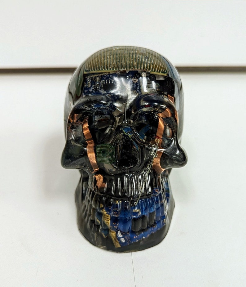 May include: A black resin skull sculpture with embedded circuit boards and copper wiring. The skull is detailed with a black resin jaw and teeth.