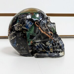 May include: A clear resin skull sculpture filled with various circuit boards and electronic components. The skull is a unique and artistic representation of technology and the human mind.