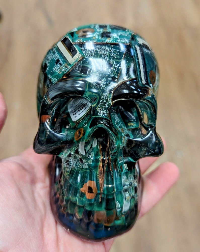 May include: A green and black skull sculpture made of resin with embedded circuit boards. The skull is detailed with a textured surface and a glossy finish.