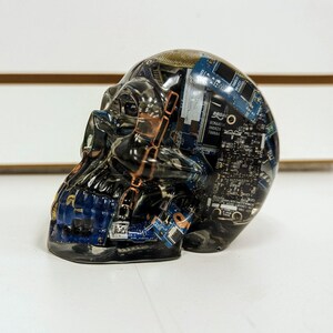 May include: A clear resin skull sculpture filled with blue and black circuit boards. The skull is a decorative object with a unique and modern design.