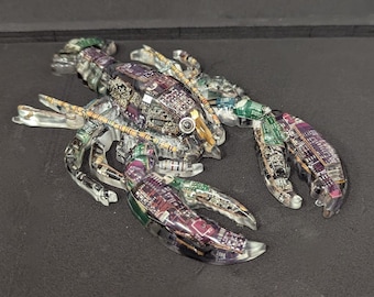 May include: A clear, detailed sculpture of a lobster, constructed from circuit board components. The lobster's body and claws are made of transparent plastic, revealing the colorful electronic parts inside. The sculpture is on a dark surface.