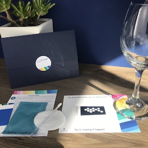 May include: A navy blue envelope with a "GOOD DROP" sticker, a wine glass with a design, and various craft supplies. The image includes a card that says "You know that dream you've always had? You're making it happen!"