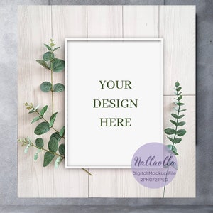 以下が含まれることがあります： 白いフレームのモックアップは、明るい木製の背景に、両側に緑の葉があります。フレームには「YOUR DESIGN HERE」というテキストが書かれています。「Nallaolla Digital Mockup File 2PNG/2JPEG」というテキストは、紫色の円の中に書かれています。