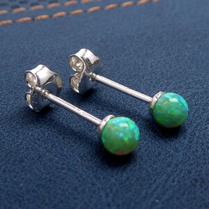 May include: A pair of silver stud earrings with green opal gemstones. The earrings have a post and butterfly back.