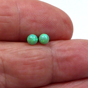 May include: A pair of green opal stud earrings. The earrings are small and round, and they have a sparkly finish.