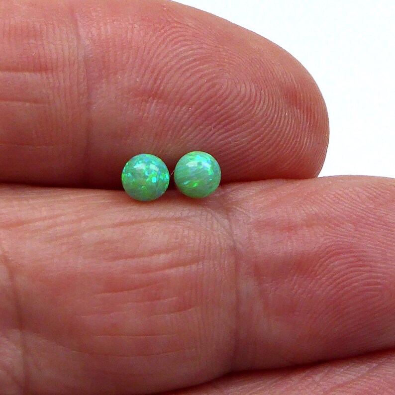 May include: A pair of green opal stud earrings. The earrings are small and round, and they have a sparkly finish.