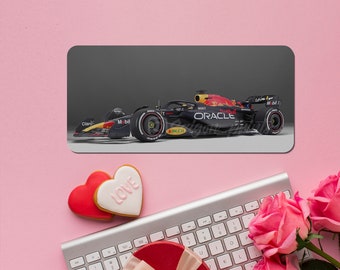 May include: A black and red race car with the word "ORACLE" on the side. The car is on a gray background. The image is surrounded by a pink background with hearts and roses.