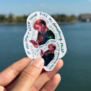 May include: Two white stickers with a woman reading, surrounded by text. The text reads "If you don't keep your eyes on something still, you can lose your balance." The stickers have a holographic effect and are held up against a blue sky.