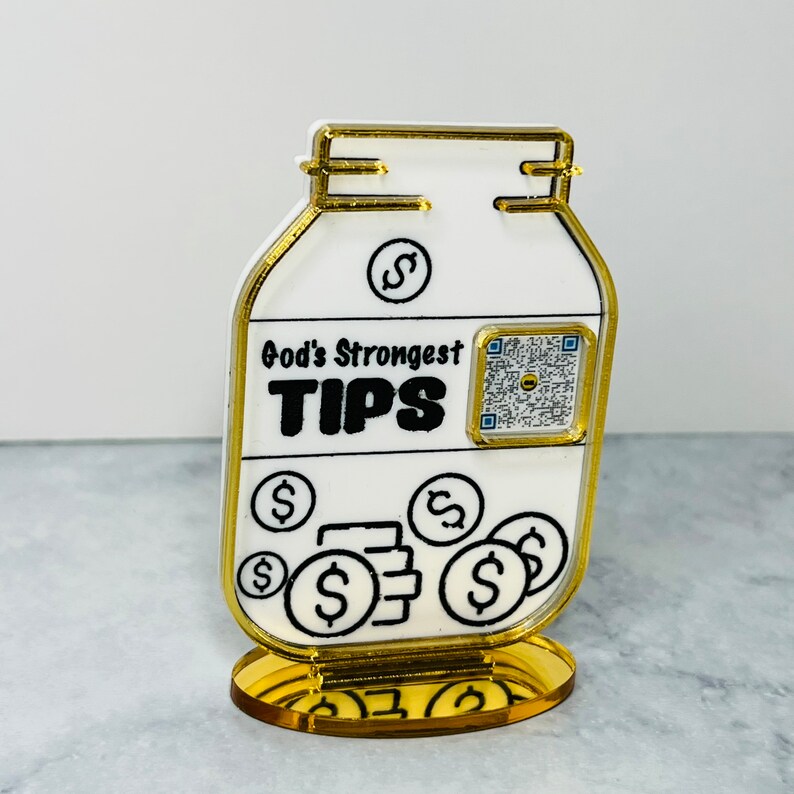 May include: A white ceramic jar with a gold rim and base. The jar has a black and white design with the text "God's Strongest TIPS" and a dollar sign. There is a QR code on the jar.