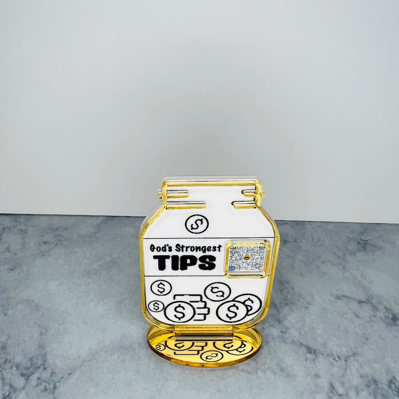 May include: A gold-colored acrylic tip jar with a white label that reads "God's Strongest TIPS". The jar is filled with gold coins and has a gold base.