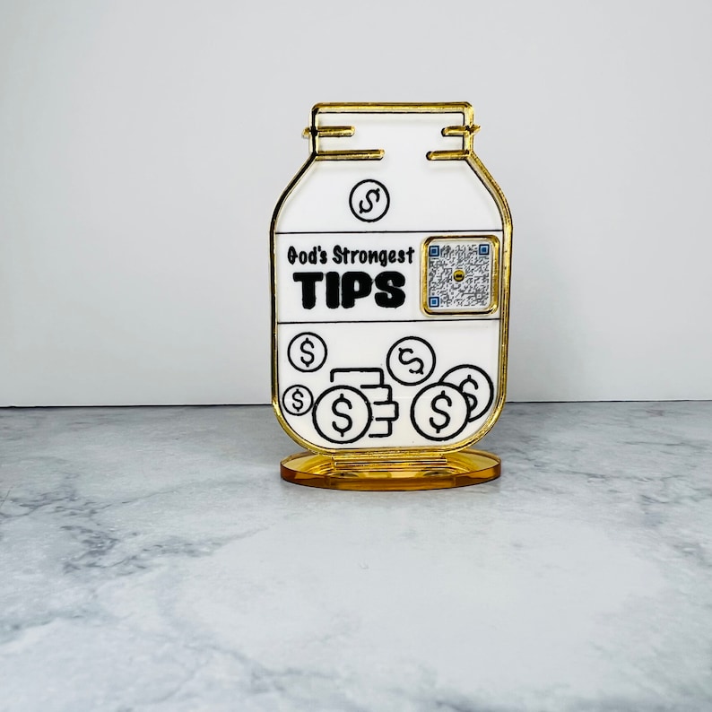 May include: A white ceramic jar with a gold rim and base. The jar has a black and white design with the text "God's Strongest TIPS" and a QR code. The jar is filled with gold dollar signs.