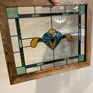 Puede incluir: Una ventana de vitrales con un diseño floral en tonos verdes, amarillos y azules. La ventana está enmarcada en un marco de madera oscura.