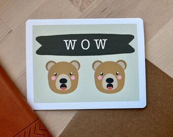 May include: A greeting card with a green background and two brown bear faces with pink cheeks. The card has a black banner with the word "WOW" in white letters.