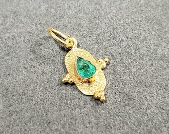 May include: A gold pendant with a pear-shaped emerald gemstone set in a textured oval frame. The frame is decorated with small gold beads.