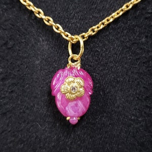 May include: A gold chain necklace with a pink flower pendant. The flower has a small clear rhinestone in the centre.