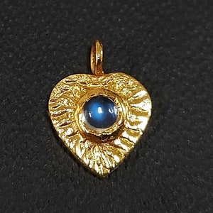 May include: A gold heart-shaped pendant with a blue gemstone in the center. The pendant has a textured surface and a loop at the top for attaching a chain.