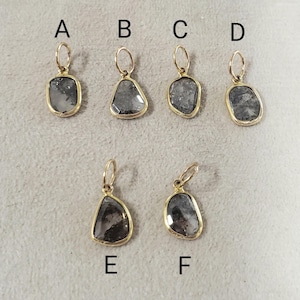 May include: Six gold earrings, each featuring a grey gemstone in an irregular shape. The gemstones are set in gold bezels. The earrings are displayed on a neutral surface.
