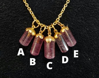 May include: A gold chain necklace with five pink and purple gemstone pendants. The pendants are labeled A, B, C, D, and E.