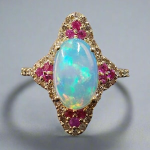 May include: A gold ring with a large oval opal gemstone surrounded by a halo of smaller diamonds and pink rubies.