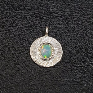 May include: A silver pendant with a textured circular design featuring a light green opal gemstone in the center.