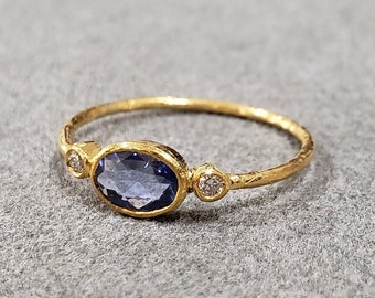 May include: A gold ring with a textured band features a blue oval gemstone and two smaller round gemstones.