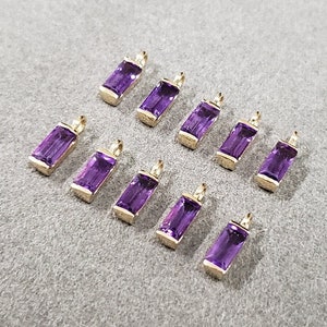 Puede incluir: Diez colgantes de amatista púrpura con engastes de oro. Los colgantes son de forma rectangular y tienen un corte facetado.