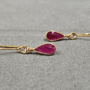 May include: A pair of gold earrings with teardrop-shaped ruby stones and smaller triangular clear stones.